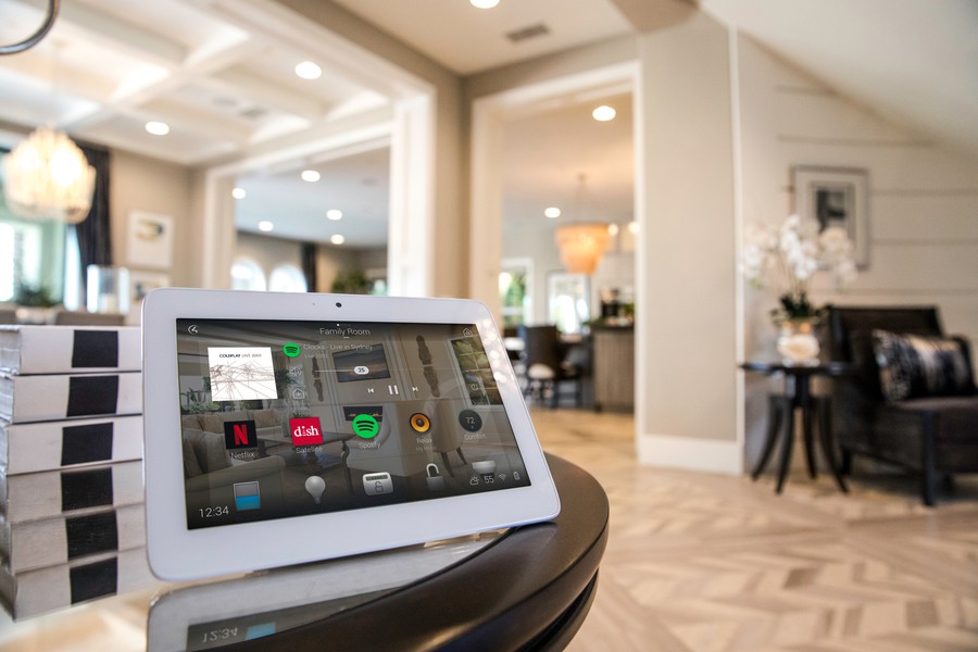 A tablet displaying Control4’s home screen with icons for Netflix, Spotify, and other apps. The tablet is placed on a table in a living room.