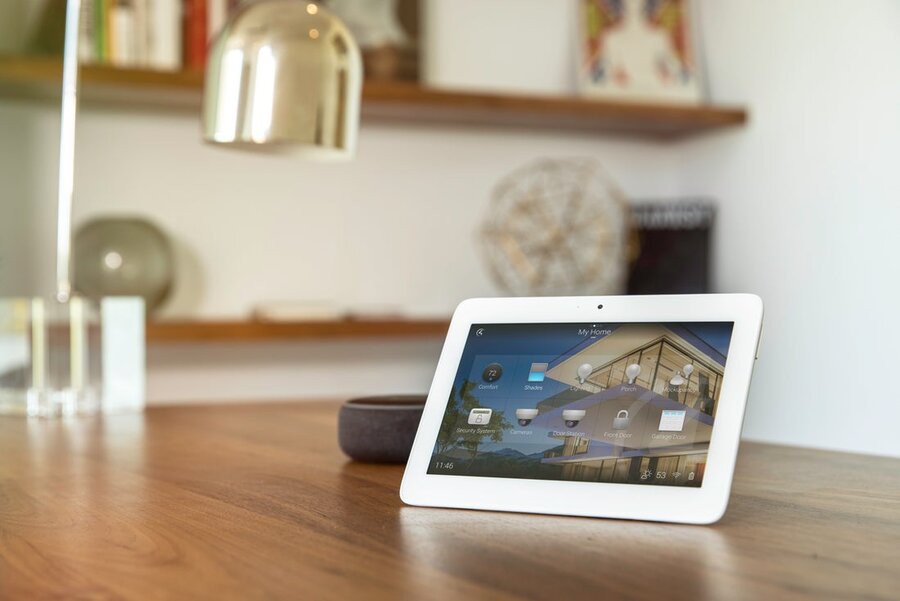 A tablet on a table with a lamp behind it, featuring the Control4 interface.